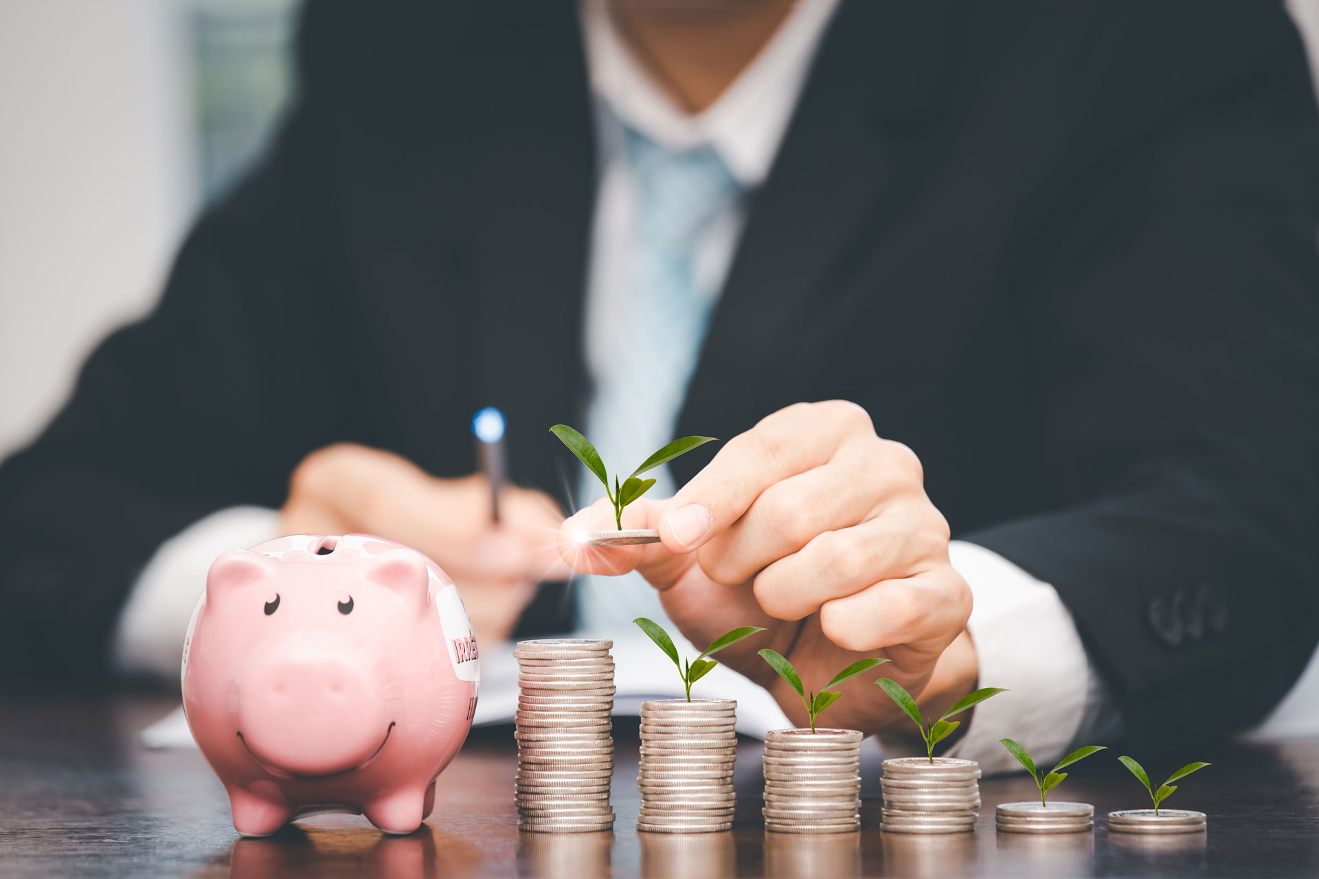 Mann mit Geldstpeln im Vordergrund und einem Sparschwein